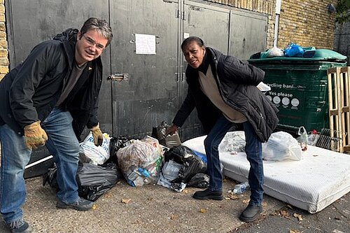 Two people pointing at fly tipped rubbish on a street