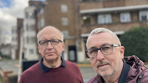 Photo of two men, councillors, in front of a housing block